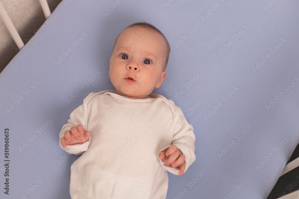 The baby is lying in his crib and looking at the camera . A happy child. Children's article.