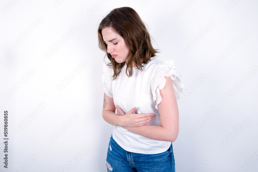 young caucasian woman wearing white T-shirt over white background  got stomachache