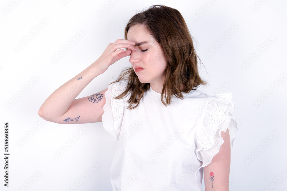 Sad young caucasian woman wearing white T-shirt over white background suffering from headache holding hand on her face Sad young caucasian woman wearing white T-shirt over white background suffering from headache holding hand on her face