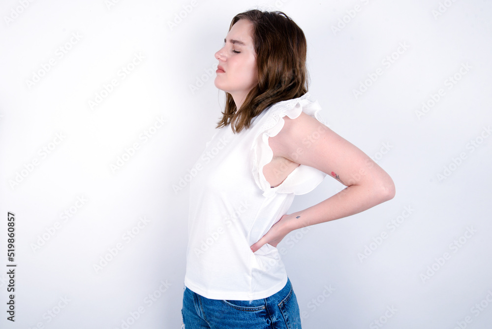 young caucasian woman wearing white T-shirt over white background got back pain young caucasian woman wearing white T-shirt over white background got back pain
