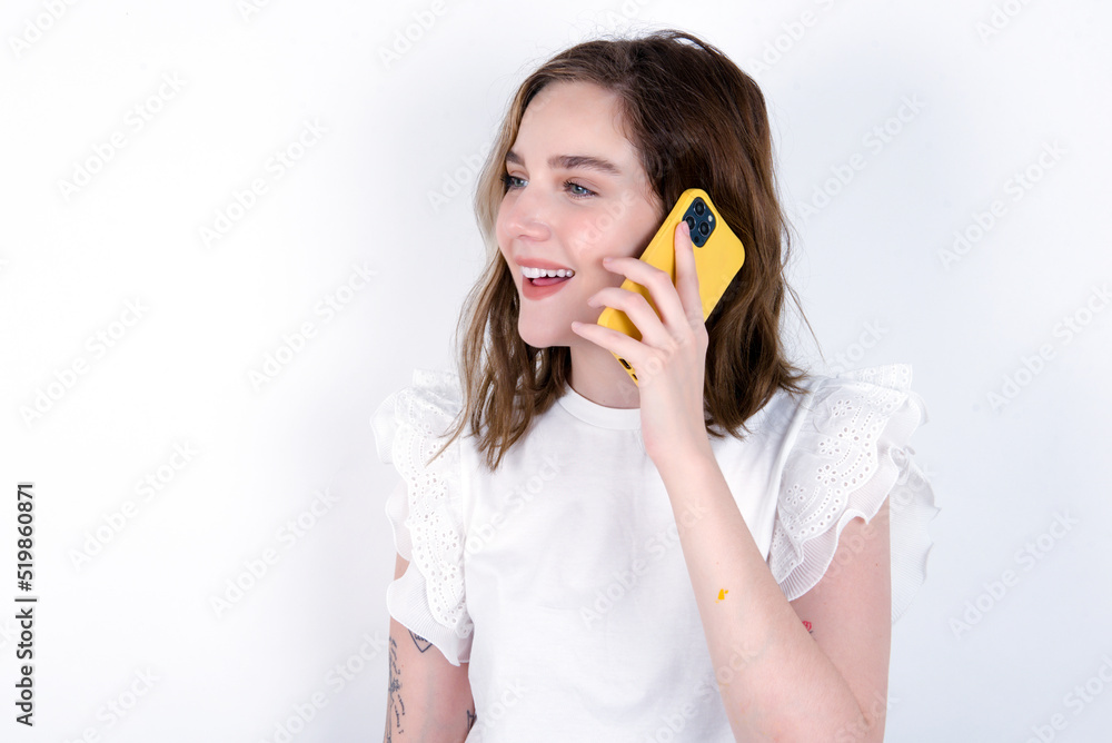Happy joyful charming young caucasian woman wearing white T-shirt over white background talk speak phone smile good mood Happy joyful charming young caucasian woman wearing white T-shirt over white background talk speak phone smile good mood