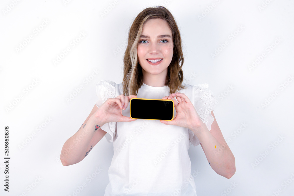 Cheerful cheery content young caucasian woman wearing white T-shirt over white background holding in hands device hobby smm post blog Cheerful cheery content young caucasian woman wearing white T-shirt over white background holding in hands device hobby smm post blog