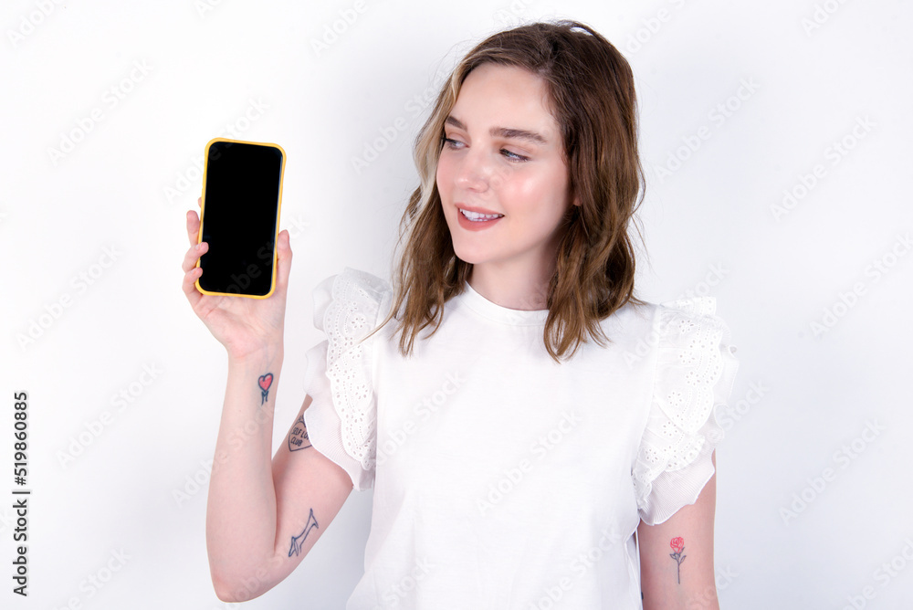 Fototapeta premium Photo of interested young caucasian woman wearing white T-shirt over white background hold telephone look side empty space screen