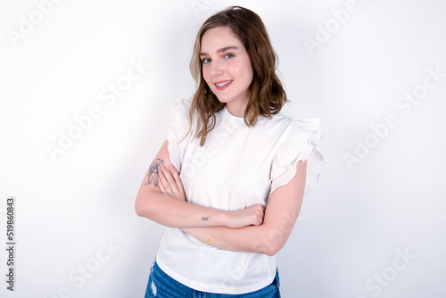 Portrait of charming young caucasian woman wearing white T-shirt over white background standing confidently smiling toothily with hands folded