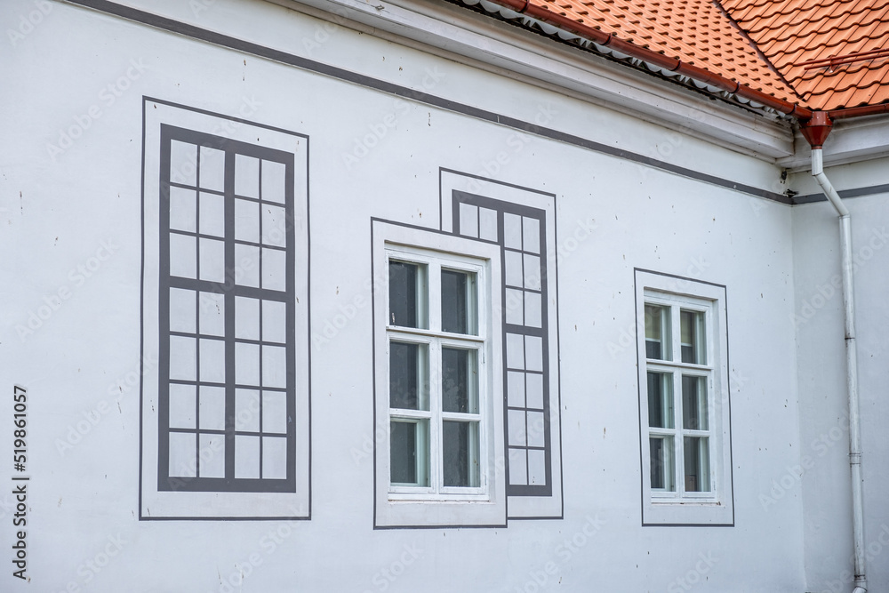 Impressive renovated white building with terracotta tiled roof and with decorative drawn windows on wall.