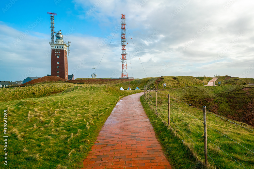 Obraz premium Golden hour by the lighthouse on the Heligoland, or Helgoland island, Germany. Cloudy sky and paved path in the front. Exploring German archipelago.