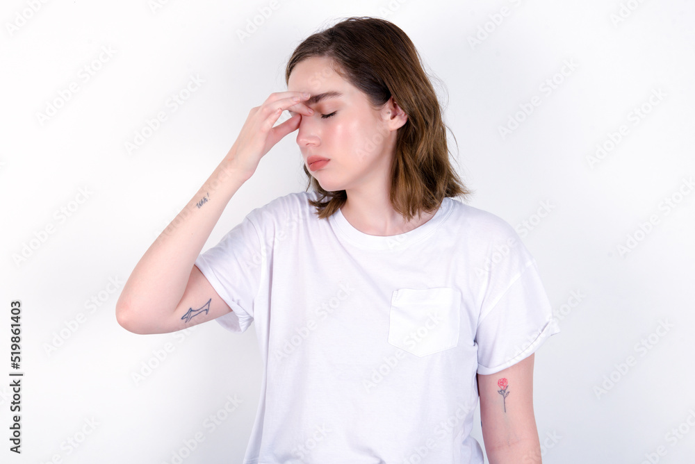 Very upset, young caucasian woman wearing white T-shirt over white background touching nose between closed eyes, wants to cry, having stressful relationship or having troubles with work Very upset, young caucasian woman wearing white T-shirt over white background touching nose between closed eyes, wants to cry, having stressful relationship or having troubles with work