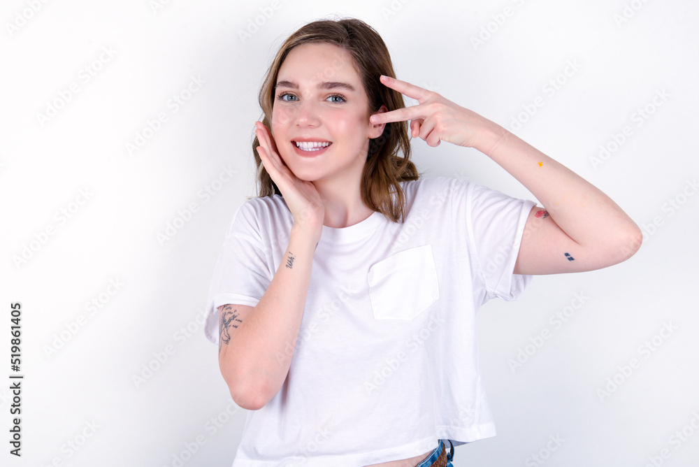 young caucasian woman wearing white T-shirt over white background making v-sign near eyes. Leisure lifestyle people person celebrate flirt coquettish concept. young caucasian woman wearing white T-shirt over white background making v-sign near eyes. Leisure lifestyle people person celebrate flirt coquettish concept.