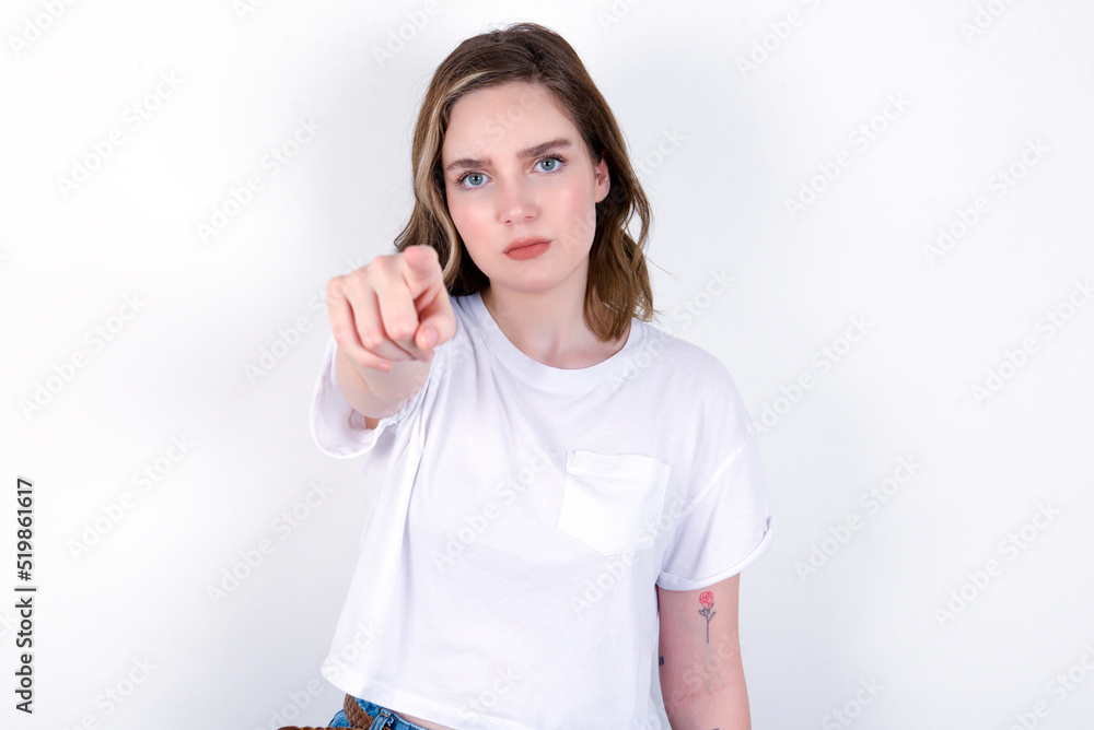 Cheerful young caucasian woman wearing white T-shirt over white background indicates happily at you, chooses to compete, has positive expression, makes choice. Cheerful young caucasian woman wearing white T-shirt over white background indicates happily at you, chooses to compete, has positive expression, makes choice.