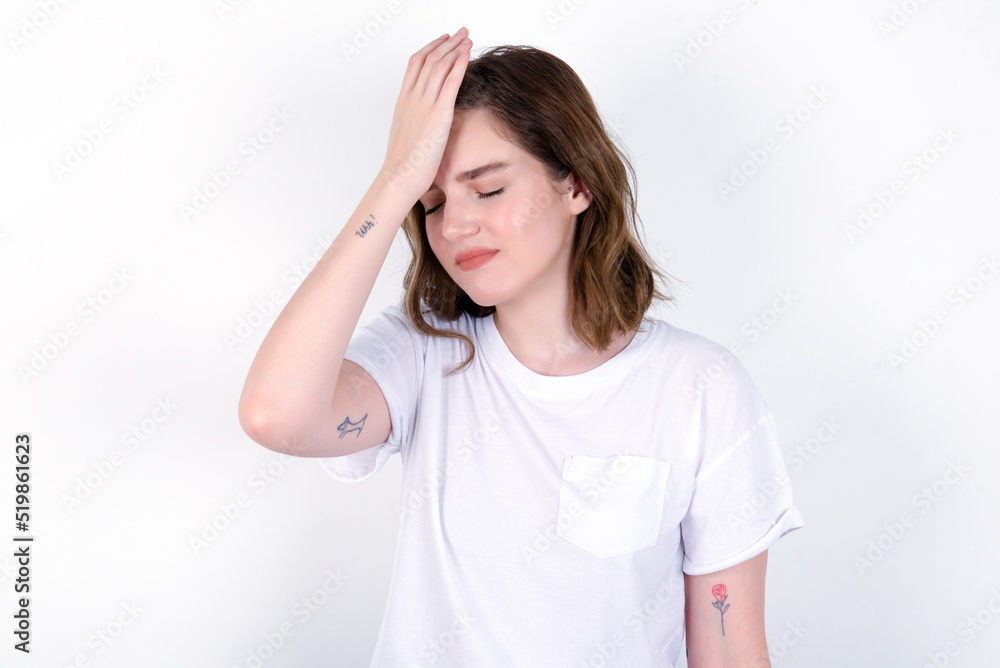 Frustrated young caucasian woman wearing white T-shirt over white background holding hand on forehead being depressed regretting what he did having headache, looking stressful. Frustrated young caucasian woman wearing white T-shirt over white background holding hand on forehead being depressed regretting what he did having headache, looking stressful.