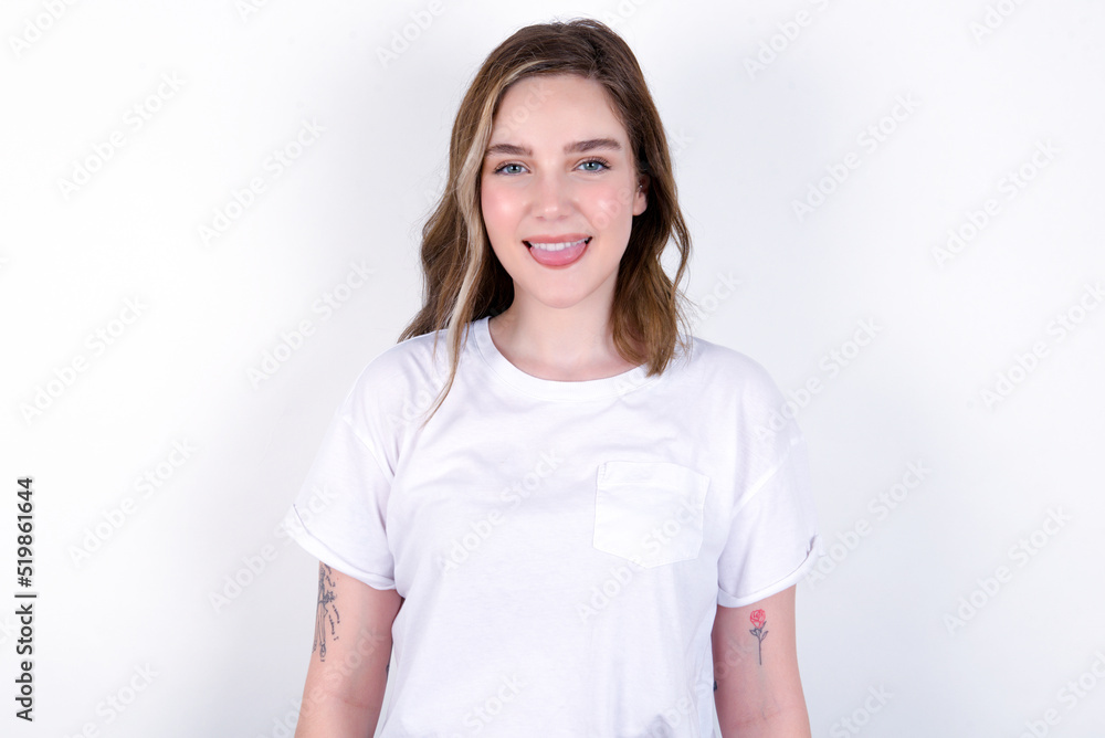young caucasian woman wearing white T-shirt over white background with happy and funny face smiling and showing tongue. young caucasian woman wearing white T-shirt over white background with happy and funny face smiling and showing tongue.