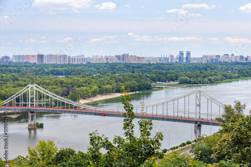 Fotografiet Beautiful cityscape of Kyiv with a view of the mountain slope, the Dnipro river with a footbridge