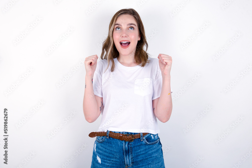 young caucasian woman wearing white T-shirt over white background champion having success being glad to achieve his goals. Victory and triumph concept. young caucasian woman wearing white T-shirt over white background champion having success being glad to achieve his goals. Victory and triumph concept.