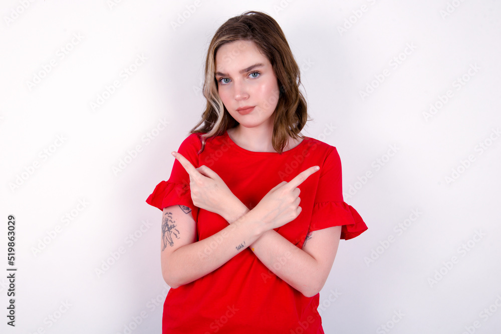 Serious young caucasian woman wearing red T-shirt over white background crosses hands and points at different sides hesitates between two items. Hard decision concept Serious young caucasian woman wearing red T-shirt over white background crosses hands and points at different sides hesitates between two items. Hard decision concept
