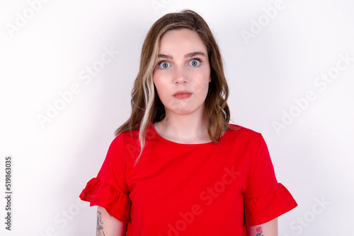 Foto Stunned young caucasian woman wearing red T-shirt over white background stares reacts on shocking news
