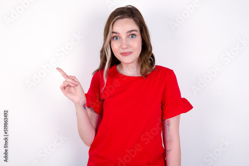 Positive young caucasian woman wearing red T-shirt over white background with satisfied expression indicates at upper right corner shows good offer suggests to click on link