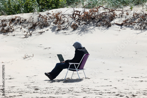 Człowiek pracuje zdalnie on line na laptopie na plaży. 