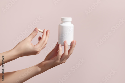 Woman holding pill and blank white plastic tube on pink background. Packaging for pill, capsule or supplement. Medic product branding mockup. photo