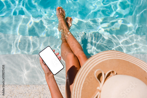 A girl by the pool holds a smartphone in her hand with a blank white display. Top view, mock up.