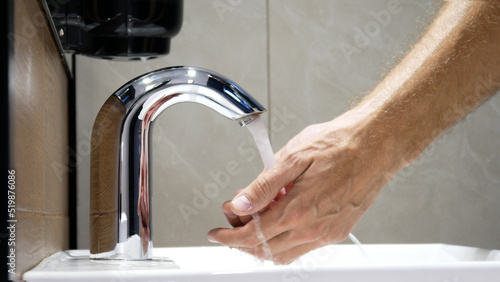 Obraz na płótnie A man washes his hands using a touchless faucet close-up