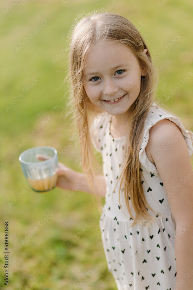 Beautiful little girl outdoors with a glass of juice looking at the camera and smiling. Close up Beautiful little girl outdoors with a glass of juice looking at the camera and smiling. Close up