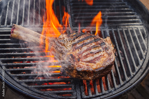 Barbecue dry aged wagyu tomahawk steak offered as close-up on a charcoal grill with fire and smoke photo