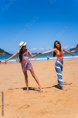 Two friends hugging on summer vacations on the beach, they are wearing a hat with the sea in the background