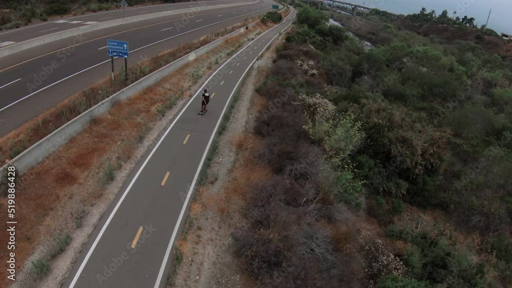Man Skateboarding down a bike path trail Man Skateboarding down a bike path trail