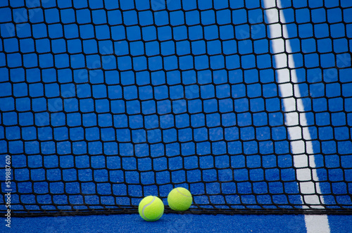 Blue paddle tennis court, two balls next to the net and the line © Vic