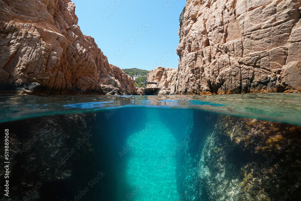 Narrow passage in rocky coast with a boat, split level view over and under water surface, Mediterranean sea, Spain, Costa Brava, Catalonia