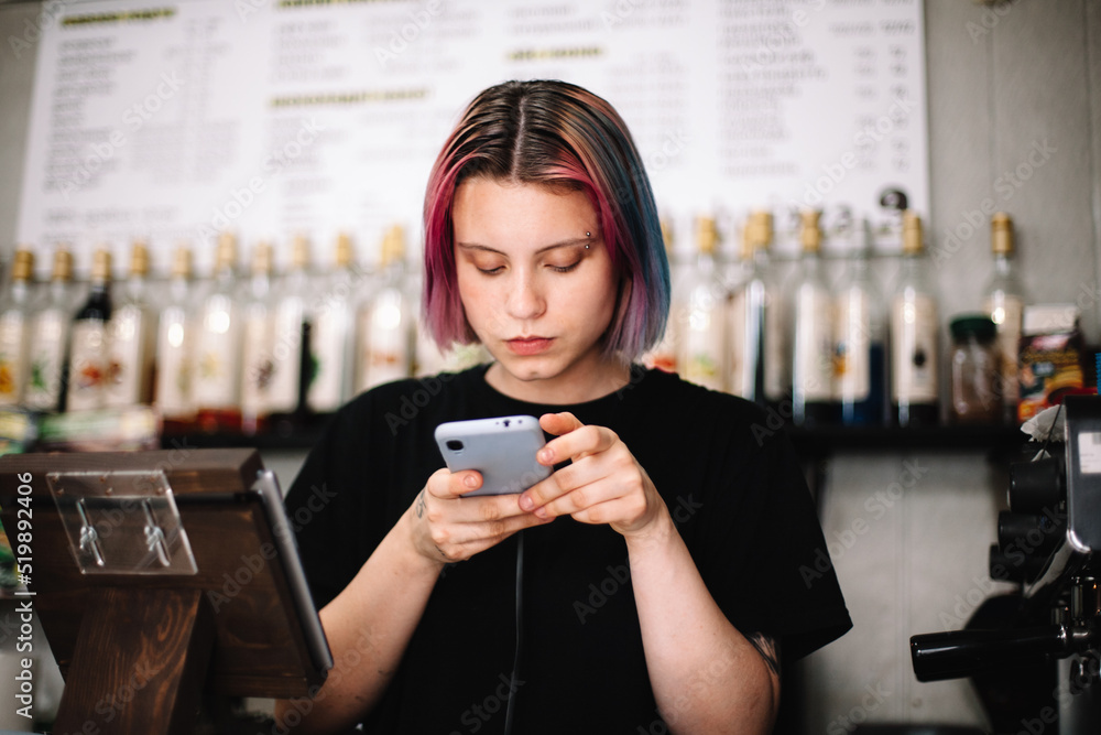 Female barista using smart phone at checkout counter in coffee shop Female barista using smart phone at checkout counter in coffee shop