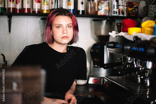 Young female barista sitting by coffee machine in coffee shop