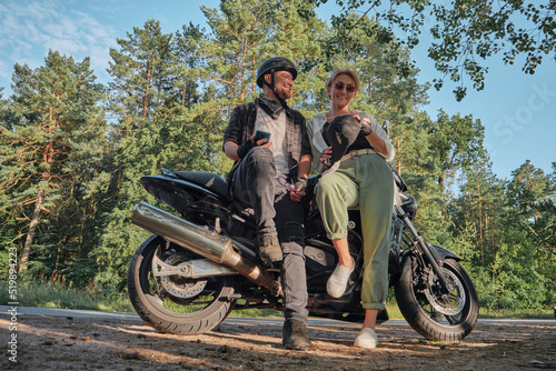 Middle age couple talking and having fun, sitting on a motorcycle, traveling together on a forest road