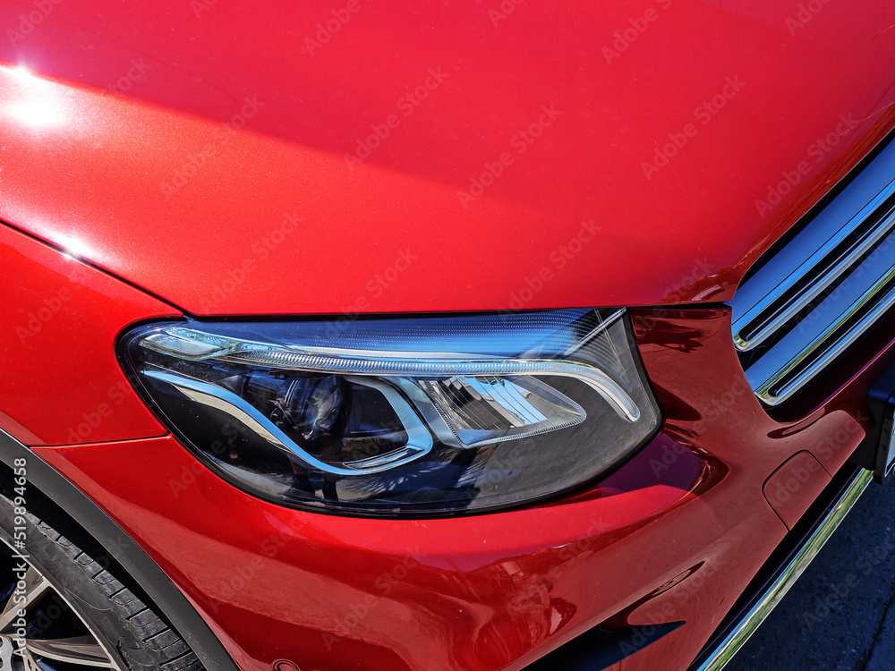 Headlight of a red new shiny car. Closeup view. Fragment of a new bright red sports car with a xenon headlight