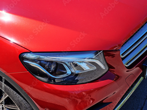 Headlight of a red new shiny car. Closeup view. Fragment of a new bright red sports car with a xenon headlight © jockermax3d