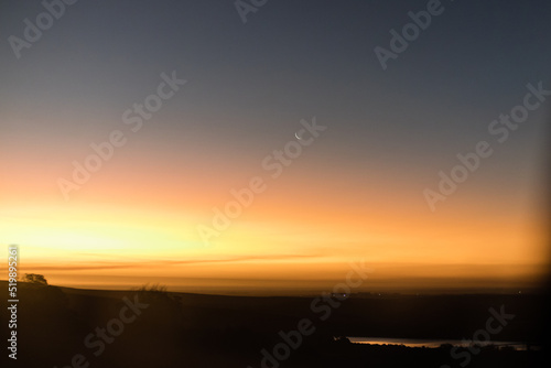 sunset in the mountains with a crescent moon with dam in the foreground