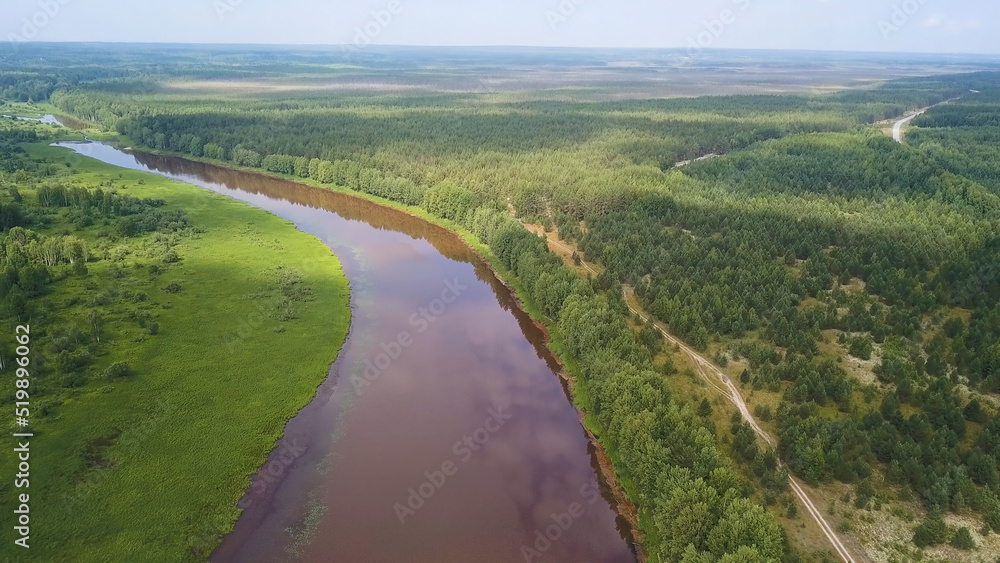 Aerial view of the river and green forest under blue sky in the summer. Clip. Summer landscape with forest, green fields and wide river on a sunny day.