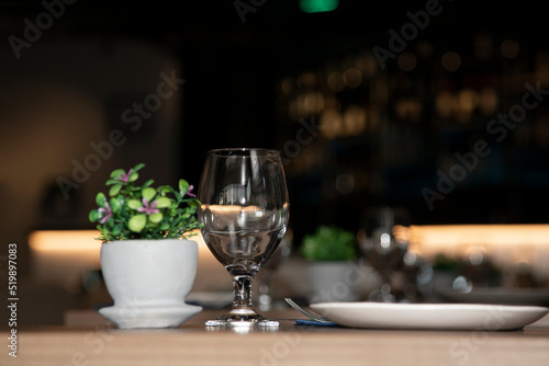 Restaurant table decorated with a small pot with flowers and a bar in the background. Decorated table in a restaurant with clean glass and plate before serving photo