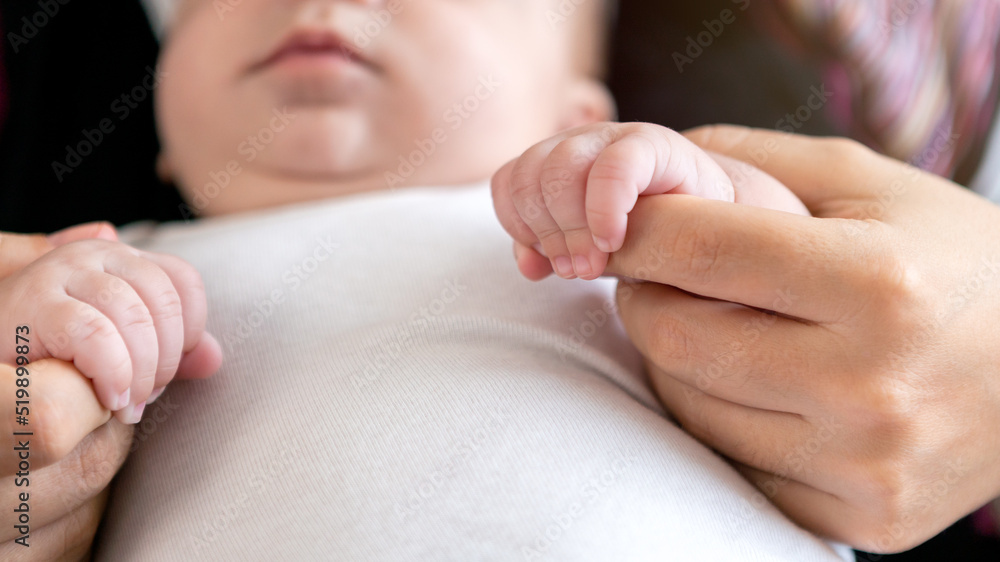 The newborn is holding a finger of mother on white sheet bed background. A baby The newborn is holding a finger of mother on white sheet bed background. A baby