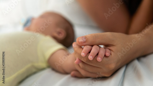 Close up mother holding hands newborn boy in a room with a lot of sunlight. Baby