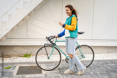 One woman young adult caucasian female walking by the university building holding bicycle and digital tablet in day real people copy space happy smile joyful full length side view