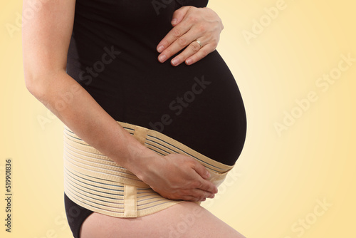 Pregnant woman with elastic maternity band on yellow background