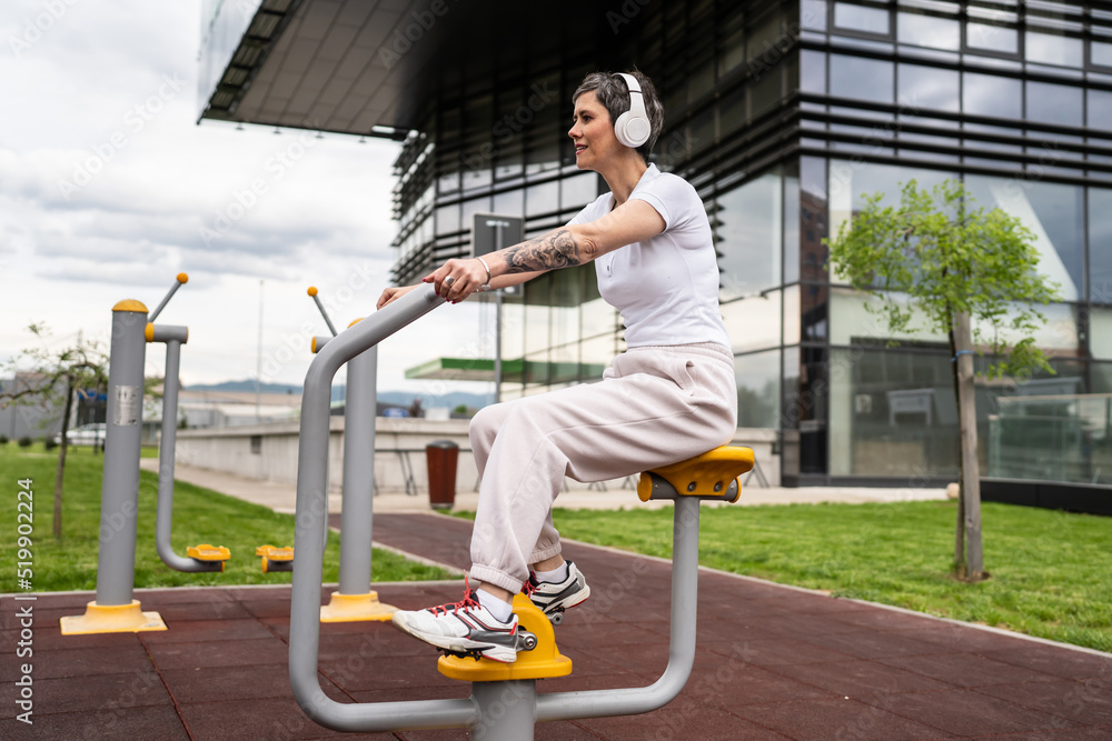 Fototapeta premium One woman modern mature caucasian female with short hair training in front of building in day on bicycle trainer machine simulator at outdoor gym Sport fitness healthy lifestyle concept copy space