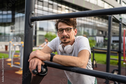 One caucasian man taking a brake during outdoor training in the park outdoor gym resting on the bars with supplement shaker in hand with water or supplementation happy smile real people copy space