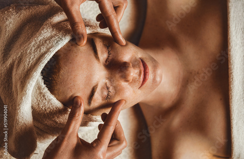 Top view of a young caucasian freckled woman having face massage in spa salon. Beautician do facial lifting massage to patient in aesthetic medicine clinic