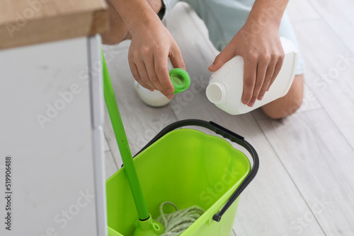 Young man pouring detergent into bucket in kitchen, closeup