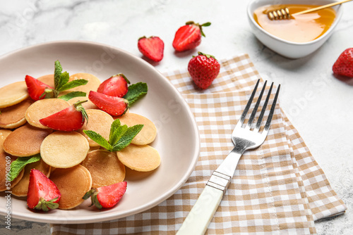 Plate of tasty mini pancakes with strawberry on light background  closeup