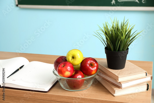 Bowl with apples, books and flowerpot on table in classroom