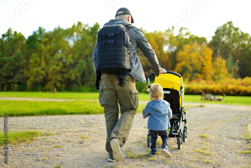 Фотография Young father walking in autumn park with toddler son in pushchair