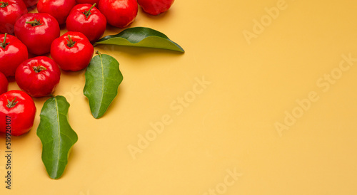 Photos Top view of ripe red acerola cherries and green leaves on a yellow background